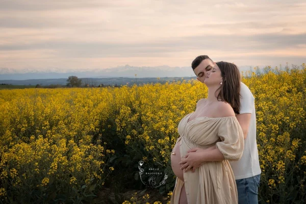 Une photo de femme enceinte entourée de fleurs de colza sur fond de chaine des Pyrénées
